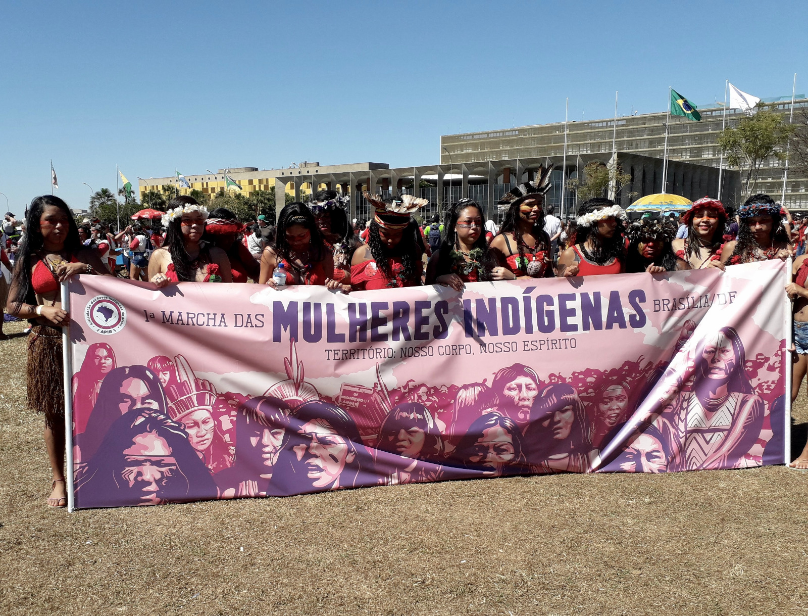 Image d'illustration montrant un groupe de femmes indigènes en manifestation. Une dizaine d'entre elles tiennent une banderole avec l'écriture "1a marcha das mulheres indigenas Brasilia"